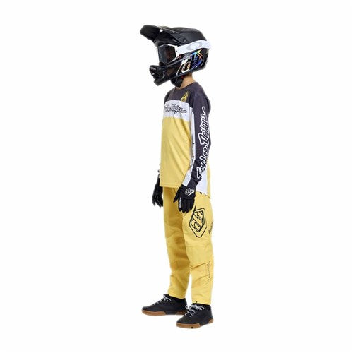 A person in profile against a white background wears TLD 26.1 Sprint Pro Pants (Youth) in Mono Butter, paired with black and yellow motocross gear, gloves, and a full-face helmet.