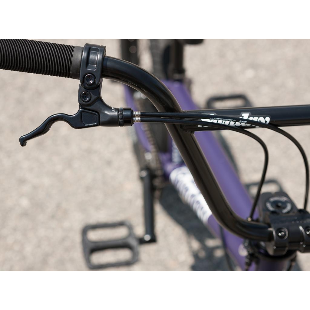 Close-up of a black handlebar with brake lever and cables, showing part of the frame, pedal, and pavement—features typical of a park BMX bike like the Sunday Forecaster Maca Grasset 20 Inch Bike, possibly with a gyro setup.