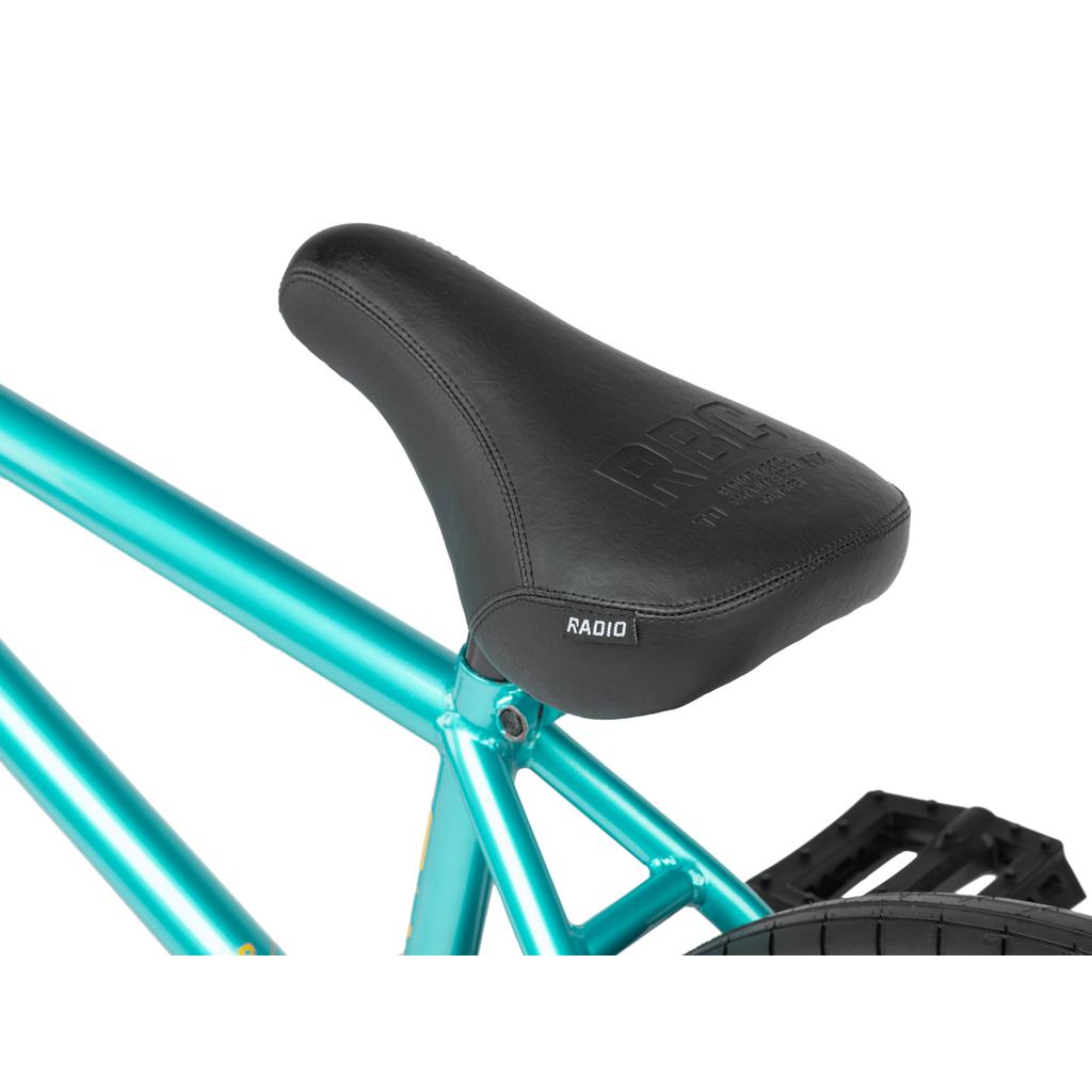 Close-up of a black seat on the Radio Darko 20 Inch Bike, featuring a metallic teal BMX design with a sturdy Chromoly frame, showing the rear wheel and pedal.