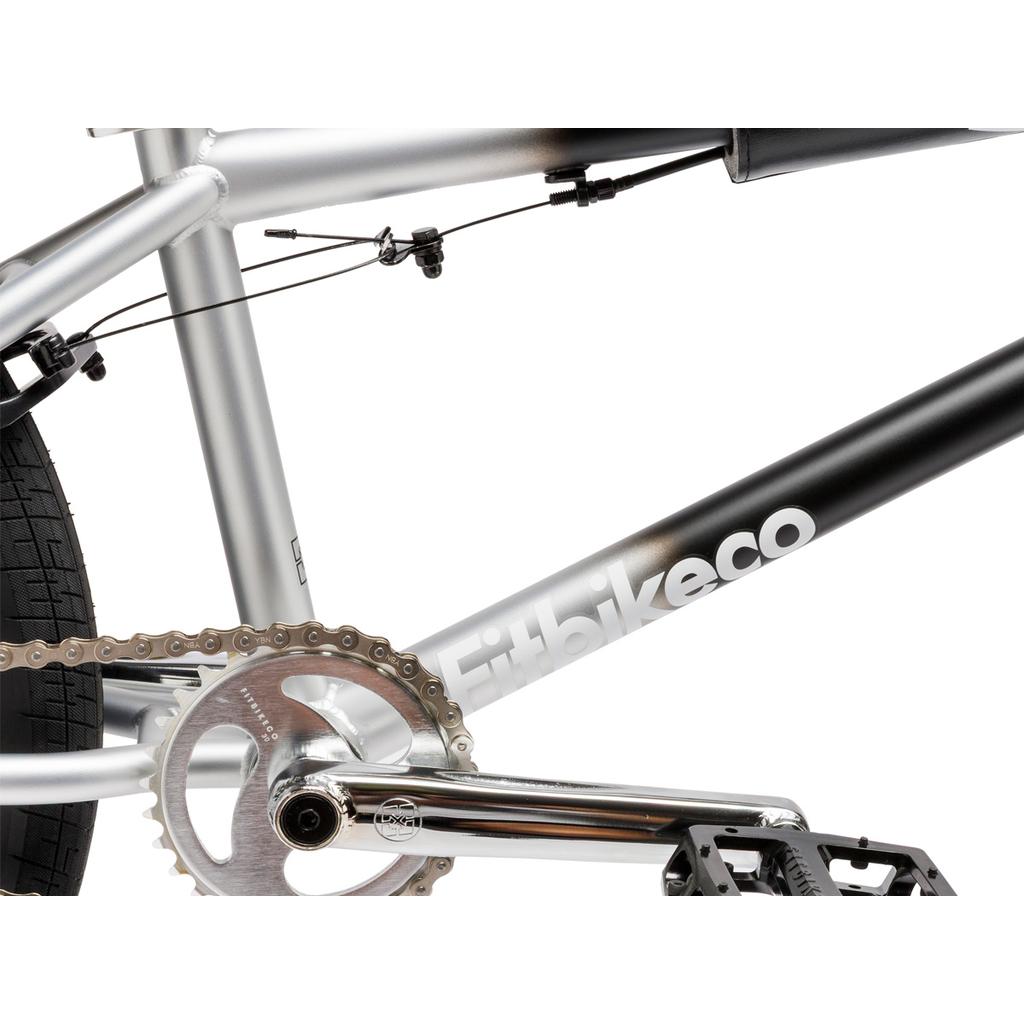 Close-up of a Fit Bike Co Series 22 Inch Bike frame in silver and black, highlighting the chain, crankset, pedal, rear tire, and brake cable.