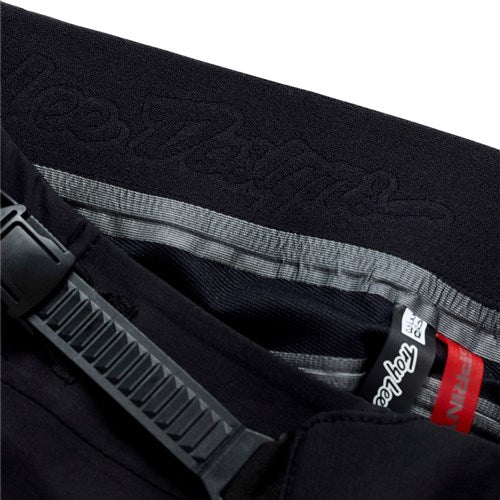 Close-up of the TLD 26.1 Sprint Ultra Pant / Mono Black BMX pants, featuring a gray stripe, plastic strap, fabric tags, and a Precision Fit perfect for downhill racing.