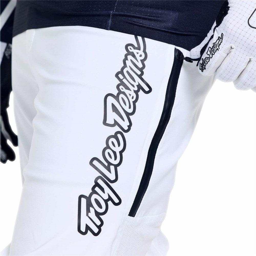 Close-up of a person wearing the TLD 26.1 Sprint Ultra Pant in Mono White, featuring "Troy Lee Designs" in black script and a visible black zipper—premium racing gear built for standout performance.