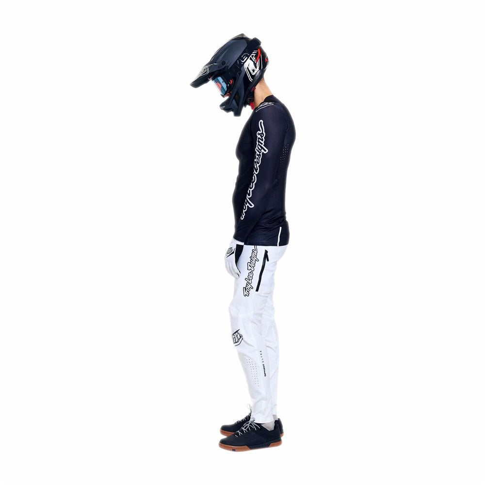Person in profile wearing a black helmet, black long-sleeve jersey, TLD 26.1 Sprint Ultra Pant / Mono White with Troy Lee racing gear’s lightweight design, and black shoes, standing against a plain white background.