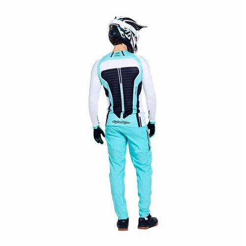 A person in teal and white protective gear, including a helmet and TLD 26.1 Sprint Ultra Pant / Mono Real Teal, stands facing away to display a back protector.