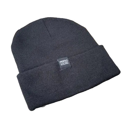 The Profile Woven Label Beanie, featuring a black knit design and "Profile Racing" woven label, rests on a weathered wooden surface.
