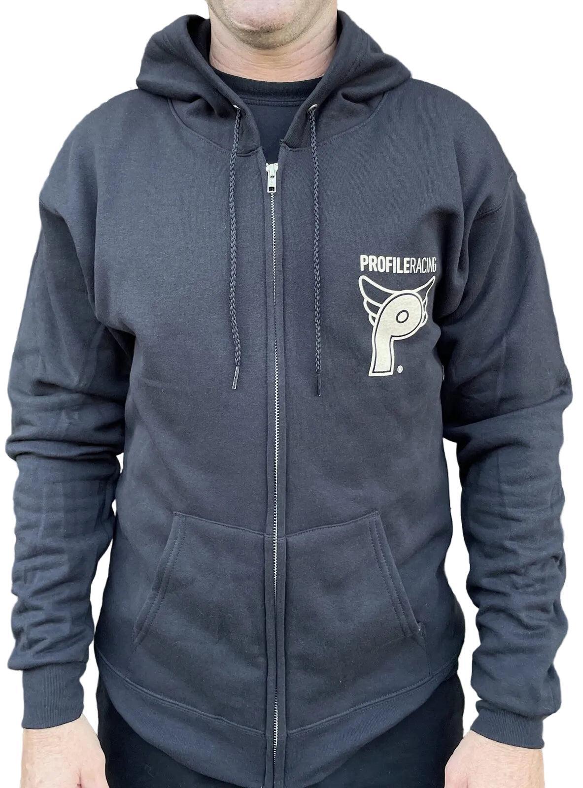 Person wearing a black Profile From the Dungeon Zip Hoodie with "Profiler Racing" logo on the left chest, standing by a fence with plants in the background.