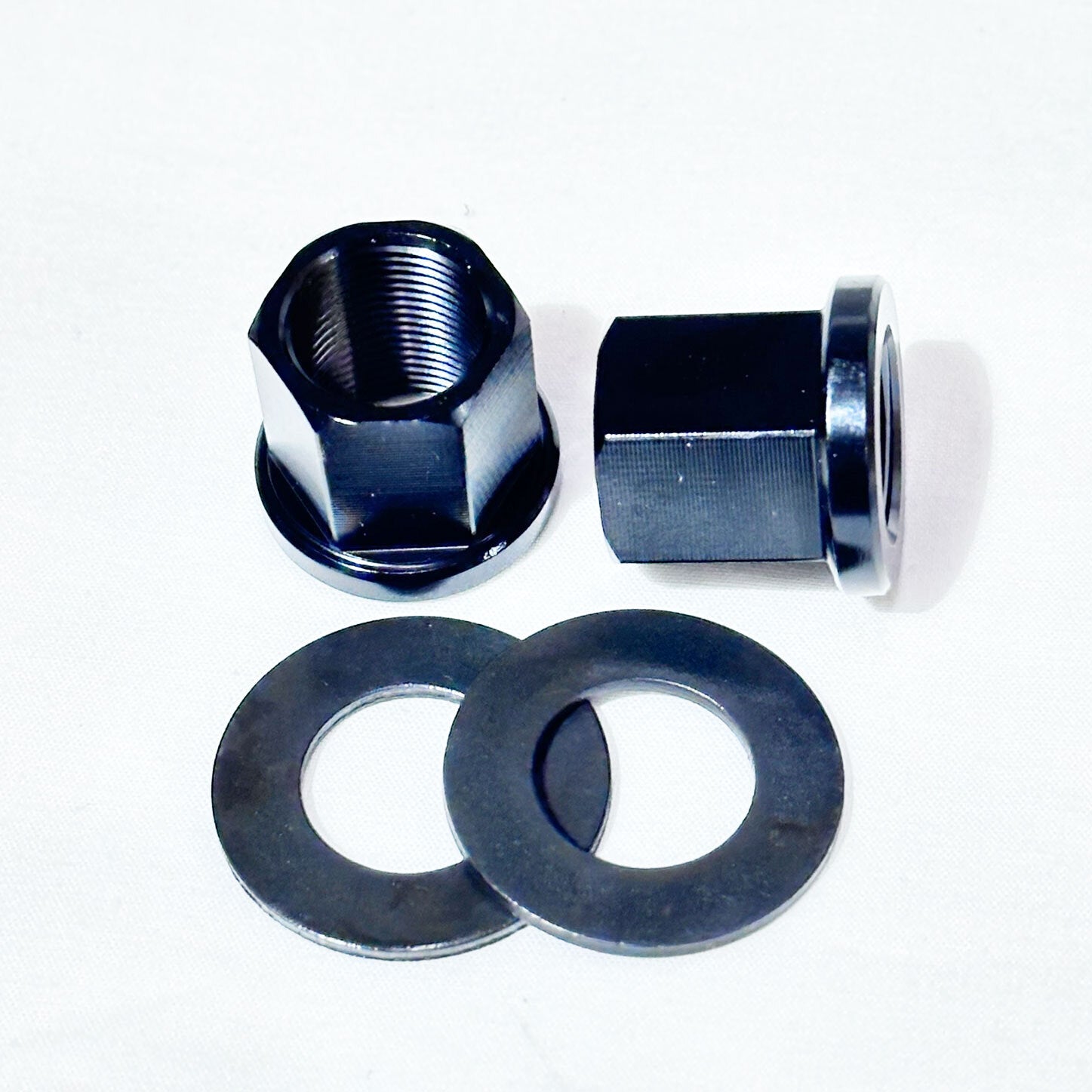 The Profile 14mm Alloy Axle Nut & Washer set, including two black alloy nuts and two flat washers, is displayed on a white surface.