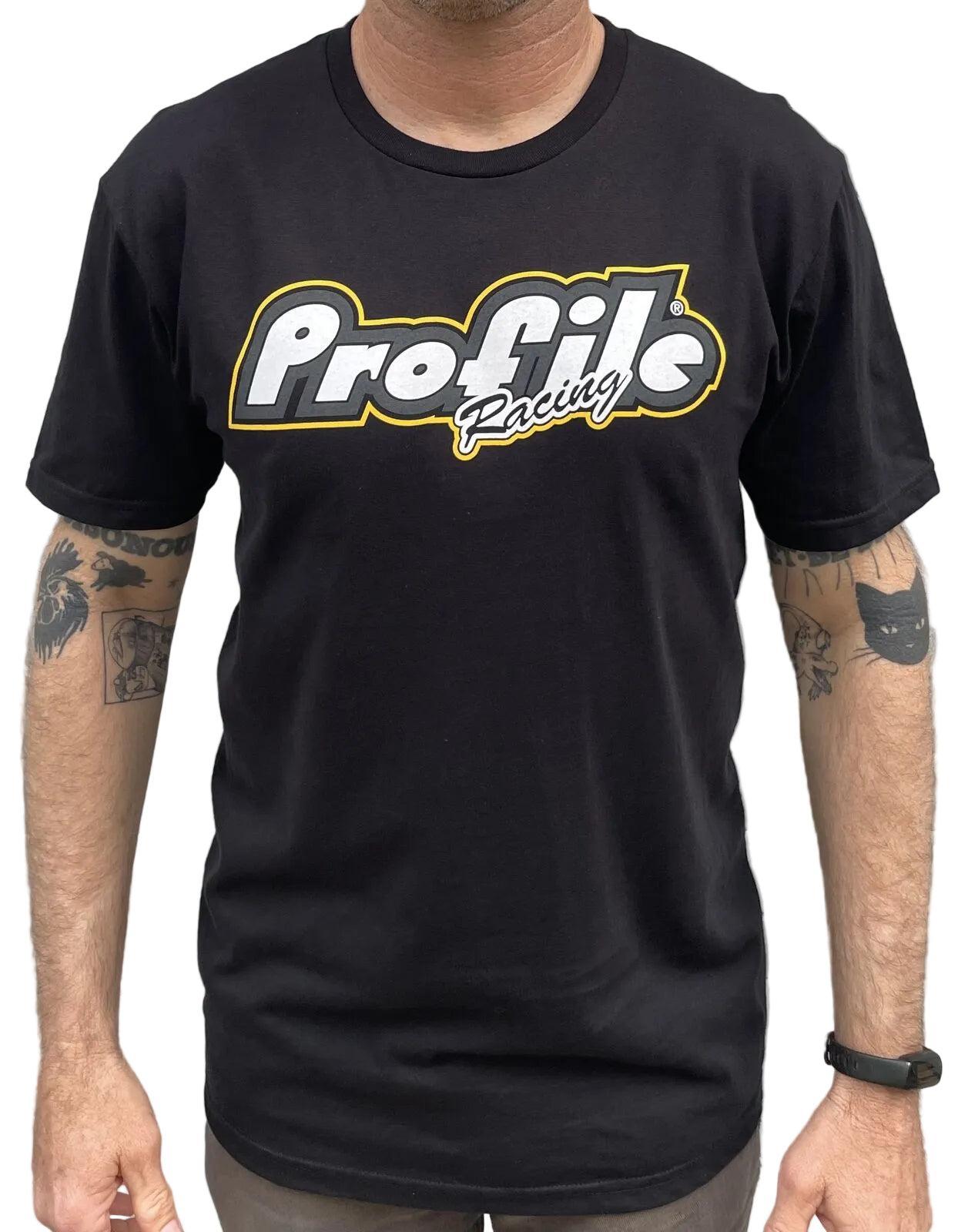 A person in a black Profile F1 Short Sleeve T-Shirt, featuring F1 Hubs, stands before a gray metal wall with tattoos visible on both arms.