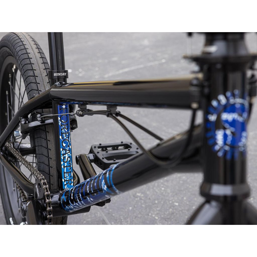 Close-up of the Sunday Forecaster Maca Grasset 20 Inch Bike in black with blue "Forecaster" graphics and "Sunday" branding near the seat post—an ideal BMX bike for your next park session, set against a concrete background.