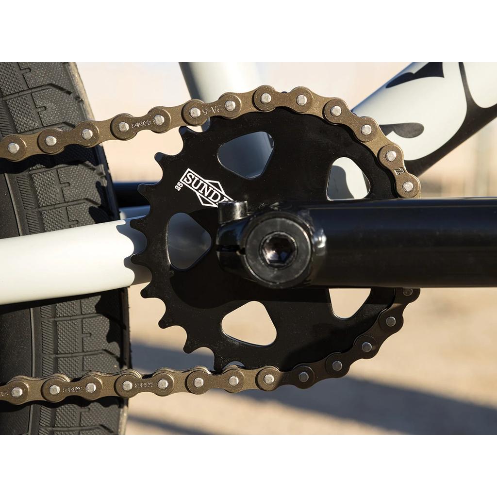Close-up of a Sunday Model C 24 Inch Bike's crankset, showing a black chainring with the "Sunday" logo, metal chain, and chromoly frame—ideal for 24” BMX builds with premium Odyssey Parts.