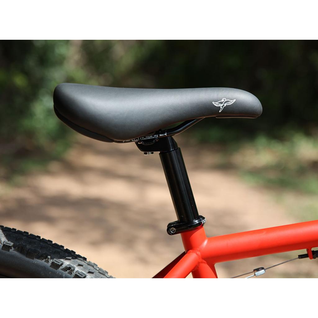 Close-up of a black bicycle seat and seatpost on a red Fairdale Taj 27.5 Inch Bike (2023) frame, perfect for BMX commuting, set against a blurred outdoor background.