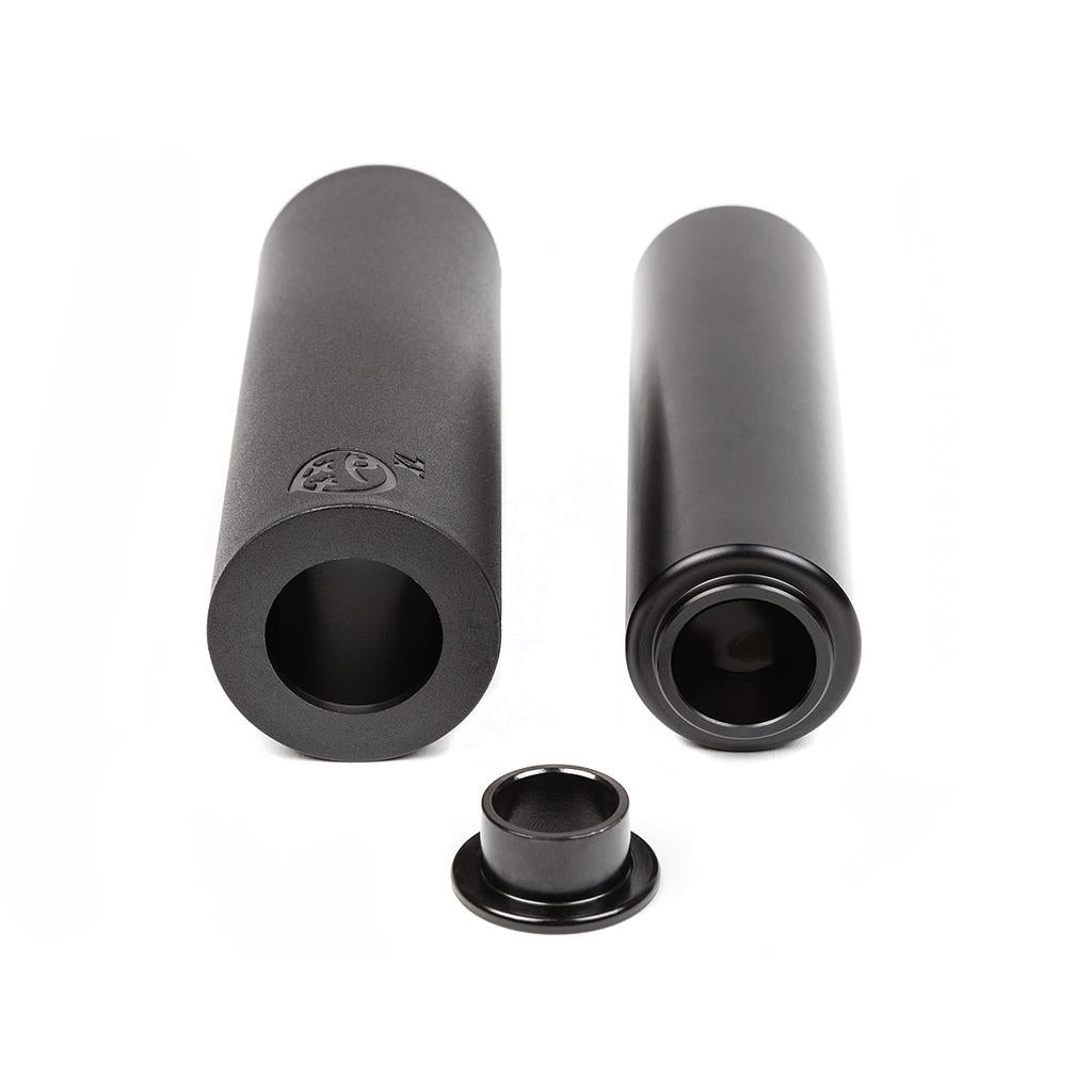 Two cylindrical black BSD Rude Tube LT V2 Plastic Pegs with hollow centers rest on a white surface, accompanied by a matching smaller ring—ideal for riders wanting a lightweight, durable bike peg option.