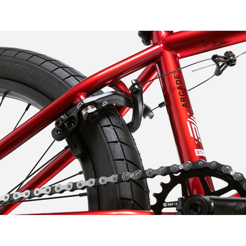 Close-up of the rear wheel, Salt Valon rims, brakes, and chain of the Wethepeople Arcade 20 Inch Bike in red, displaying part of the frame with “ARCADE” and detailed mid-tier BMX components.