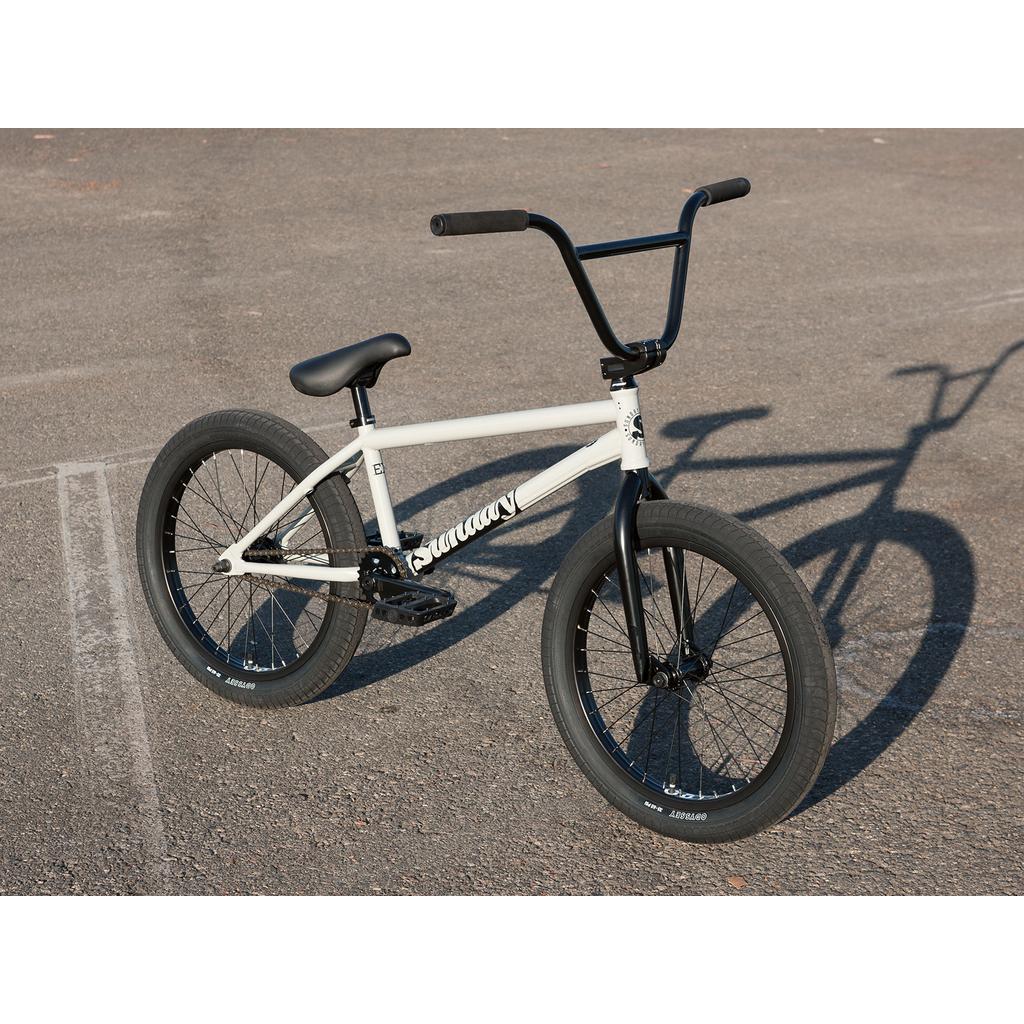 A Sunday EX Erik Elstran 20 Inch Bike with a 100% chromoly frame and thick tires in white and black is parked on an empty asphalt surface.