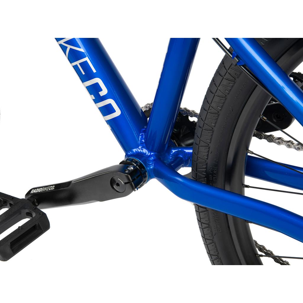 Close-up of the Radio Fiend 26 Inch Bike frame in blue, crafted from strong 6061-T6 alloy, highlighting the crank arm, pedal, and rear tire on this dirt jump bike.