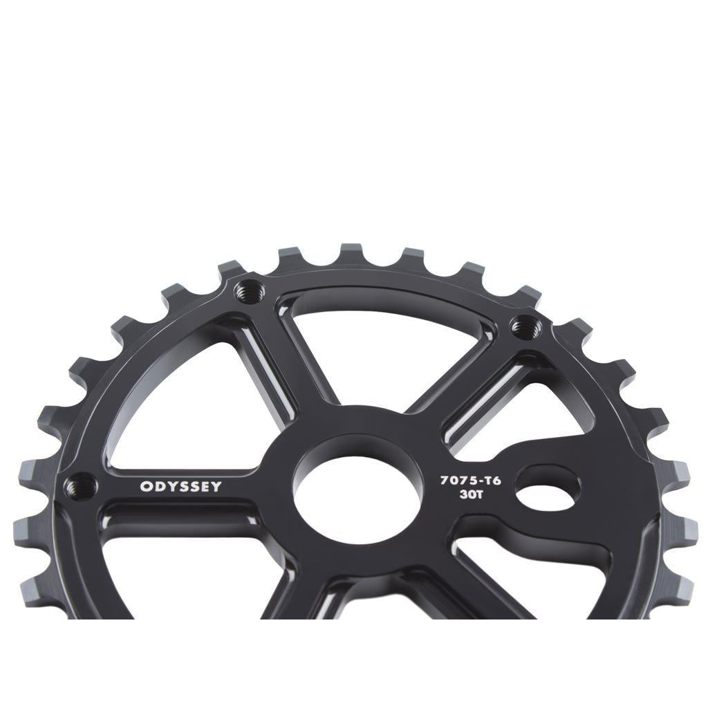 Close-up of a black metal Odyssey Utility Pro Sprocket, featuring 7075-T6 30T marking, with visible gear teeth and a cutout design shown against a white background.