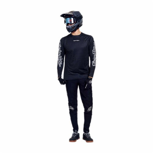 Person wearing black motocross gear, including a TLD 26.1 Sprint Pro Jersey / Mono Black with moisture wicking properties, helmet, goggles, long-sleeve shirt, gloves, and pants, standing against a white background.