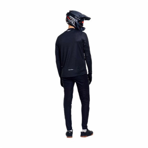 A person in a black motocross helmet, TLD 26.1 Sprint Pro Jersey / Mono Black, pants, gloves, and shoes stands facing away from the camera against a white background.