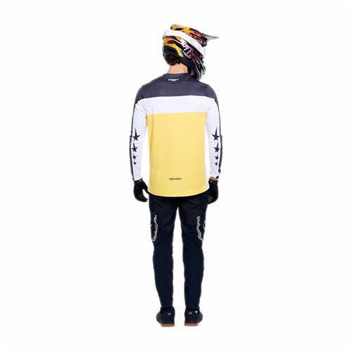 Person wearing a motocross helmet, TLD 26.1 Sprint Pro Jersey / Yo Moto Butter with moisture-wicking fabric, black gloves, and black pants, standing facing away against a white background.