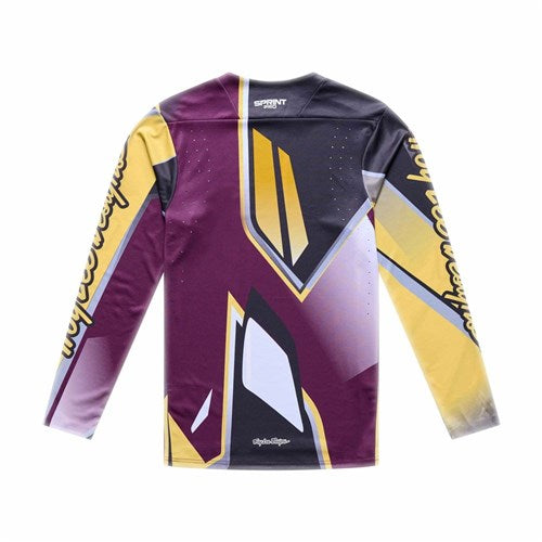 The TLD 26.1 Sprint Pro Jersey / Lowrider Sangria is a long-sleeve athletic jersey with a geometric purple, yellow, black, and white pattern, text on the sleeves, back ventilation holes, and moisture-wicking fabric for intense rides.