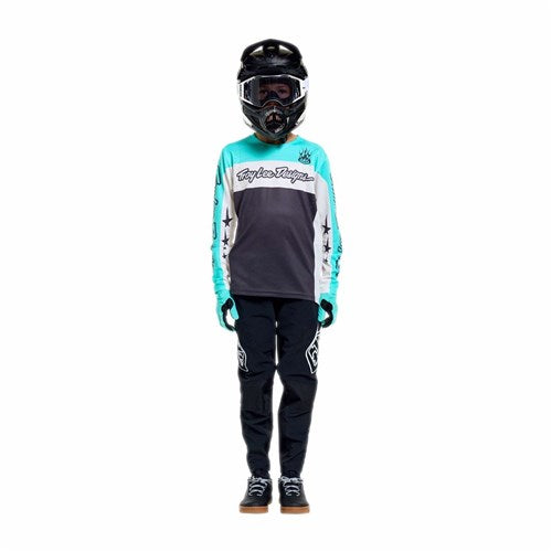 Person standing facing forward, wearing a full motocross outfit with a TLD 26.1 Sprint Pro Jersey (Youth) in Yo Moto Carbon, black race-fit pants, helmet, and gloves, isolated on a white background.