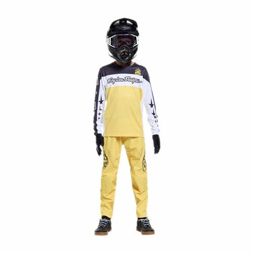 A person wearing a black helmet, goggles, gloves, and the TLD 26.1 Sprint Pro Jersey (Youth) in Yo Moto Butter stands against a plain white background.