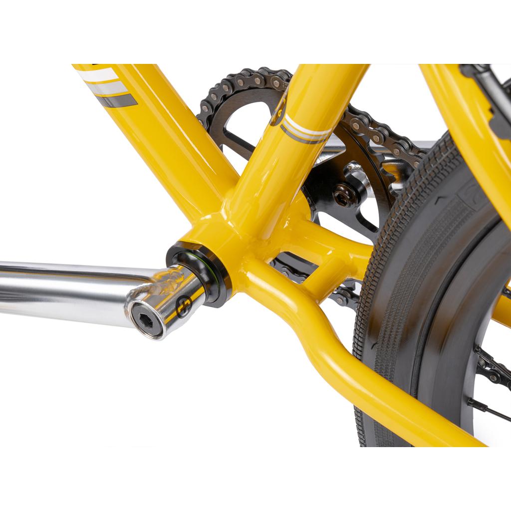 Close-up of the Wethepeople Atlas 24 Inch Bike's yellow crank arm, bottom bracket, chainring, and rear wheel tire, showcasing its classic cruiser design and durable 24" wheels.