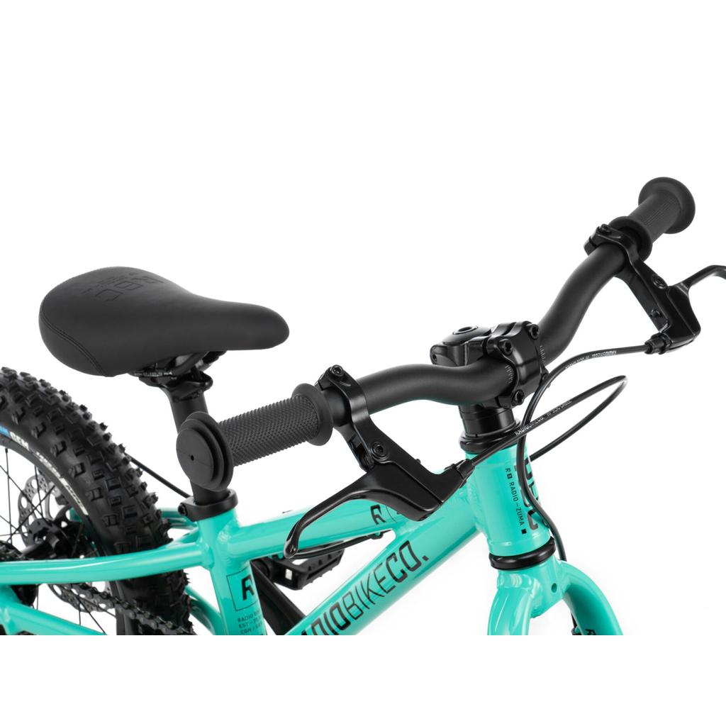 Close-up of the Radio Zuma 14 Inch Bike’s turquoise frame, seat, handlebars with black grips, brake levers, and tire tread—designed as a lightweight mountain bike ideal for young riders.