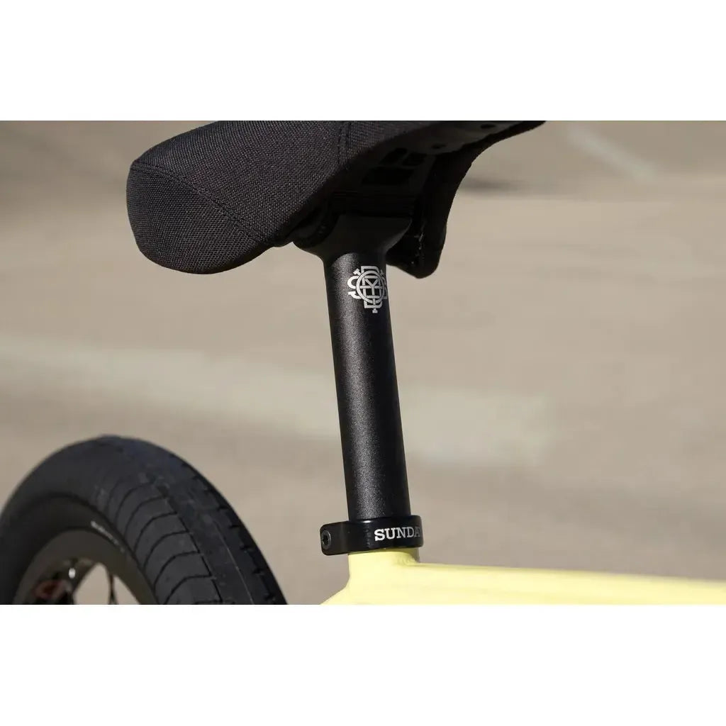 Close-up of the Sunday Soundwave Special Bike (2025) seat, seat post with white graphic and "SUNDAY" clamp, and rear wheel against a blurred outdoor background—featuring quality Odyssey parts with 41-Thermal Lifetime Warranty.