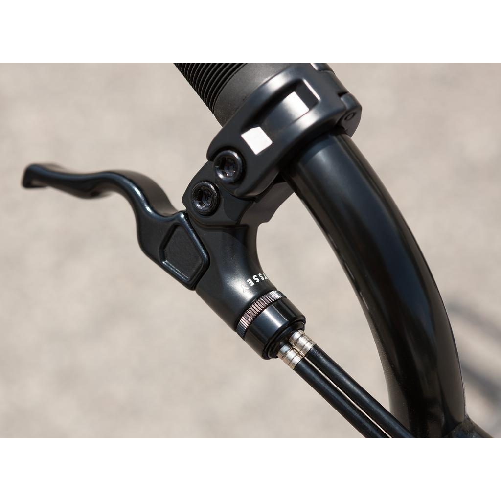 Close-up of the black brake lever and handlebar with adjustment dial and cable on the Sunday Forecaster Maca Grasset 20 Inch Bike, highlighting its park BMX gyro setup against a blurred background.