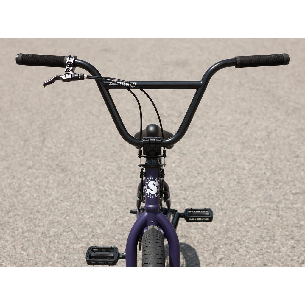 Front view of the Sunday Forecaster Maca Grasset 20 Inch Bike showing handlebars, gyro setup brake lever, front tire, and pedals on a paved surface.