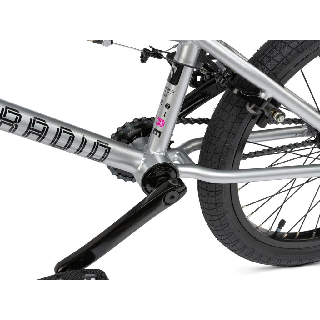 Close-up of the Radio Revo Pro 20 Inch Bike’s silver frame, highlighting the Rookie Three Piece Cranks, chain, crank arm, and rear wheel with textured tire and visible brake mechanism.