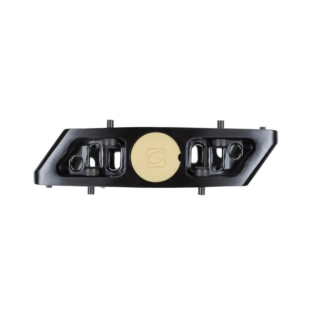 The Odyssey Trail Mix Loose Ball Pedals feature a black rectangular aluminum body with two side cutouts and a central beige circular element, shown from above on a white background.
