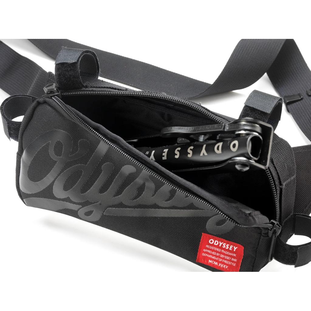 An unzipped ODYSSEY Switch Pack V2 Hip Bag reveals a compact black bike tool inside, with a red label featuring white text attached to the bag's exterior.