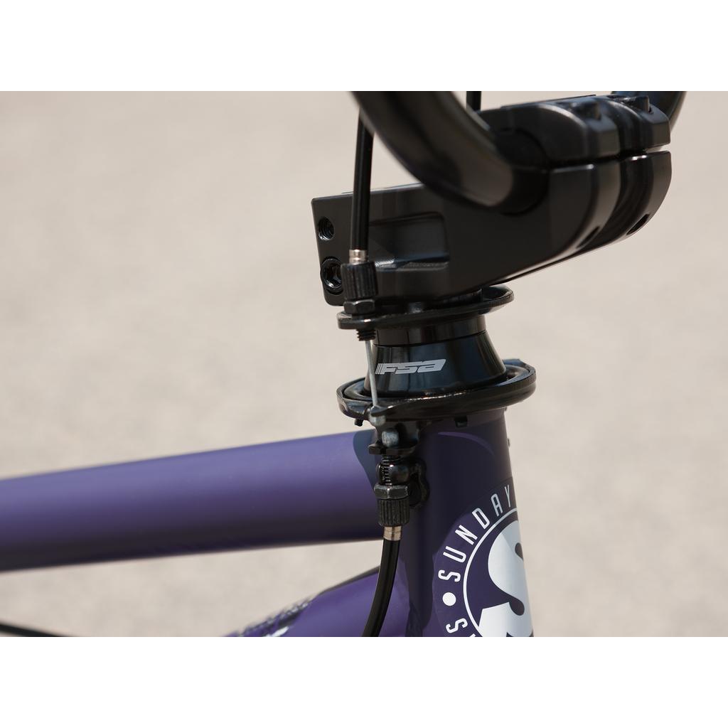 Close-up of the Sunday Forecaster Maca Grasset 20 Inch Bike’s purple frame, black handlebars, headset with visible brake cables, park bike gyro setup, and “FSA” logo.