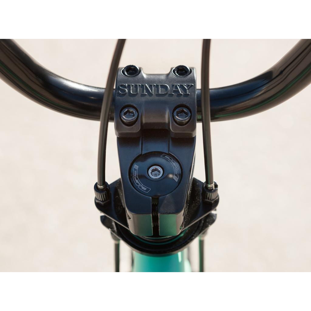 Close-up of the Sunday Primer Park 20 Inch Bike handlebar stem with "SUNDAY" engraving, visible bolts, partial handlebar, and elements of its BMX gyro setup.