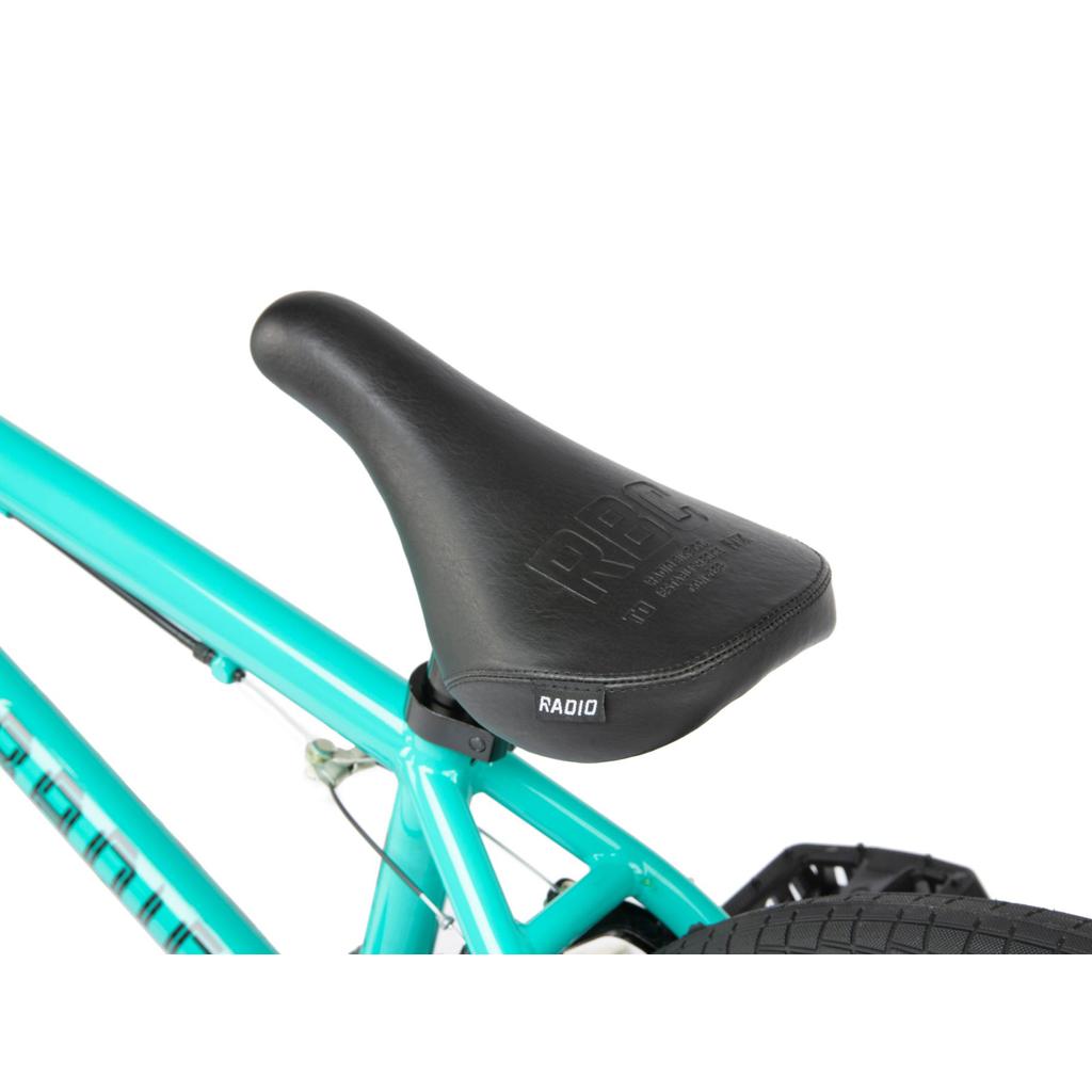 Close-up of a black RADIO bicycle seat on a turquoise Radio Revo Pro FS 20 Inch Bike, showing the 20-inch top tube and part of the rear tire.