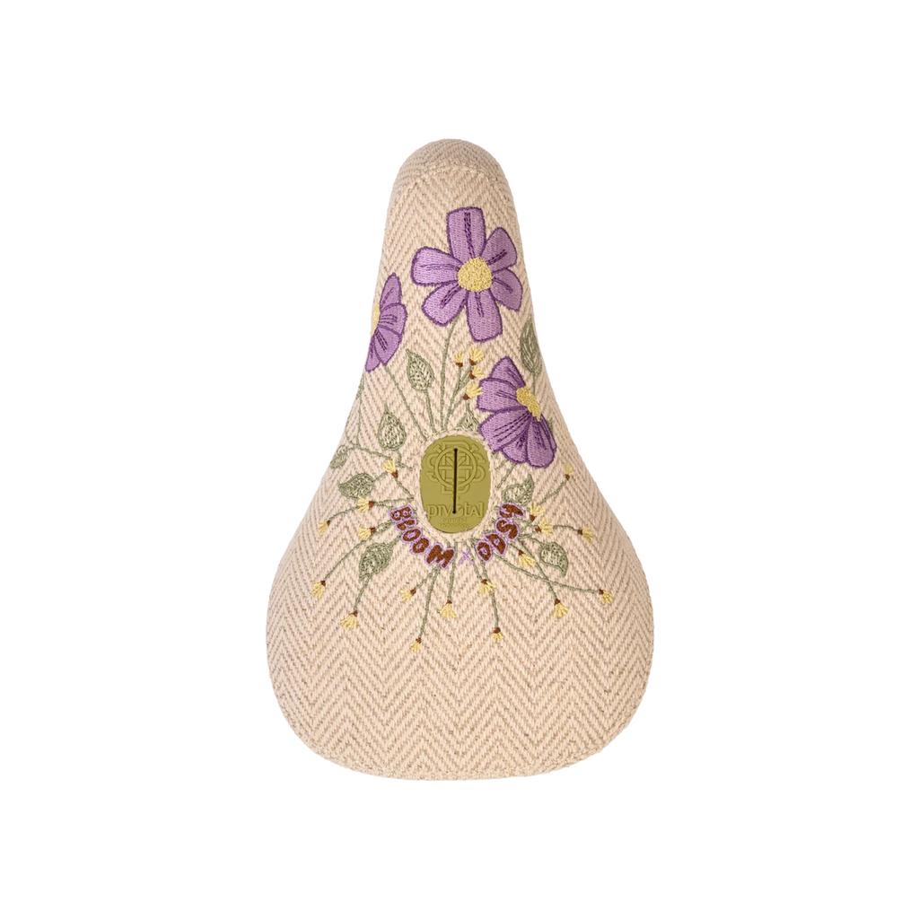 The Odyssey Bloom V2 Pivotal Seat is beige with a herringbone pattern, embroidered purple flowers, and a gold "Bloom Daisy" emblem.
