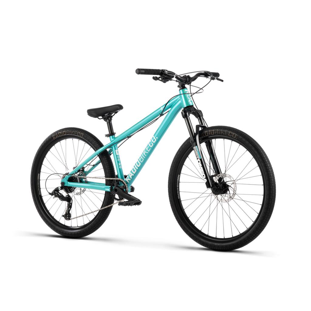 A teal Radio Fiend 26 Inch Bike with a 6061-T6 alloy frame, front suspension, flat handlebars, disc brakes, and knobby tires is displayed on a white background.