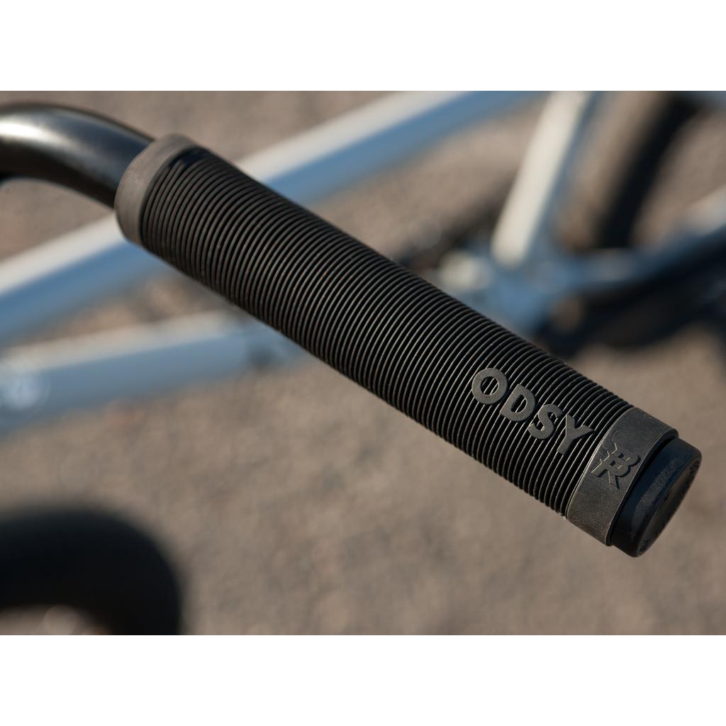 Close-up of a black ribbed handlebar grip with "ODSY" branding on a metal handlebar, attached to the Sunday EX Erik Elstran 20 Inch Bike, which features a 100% chromoly frame.