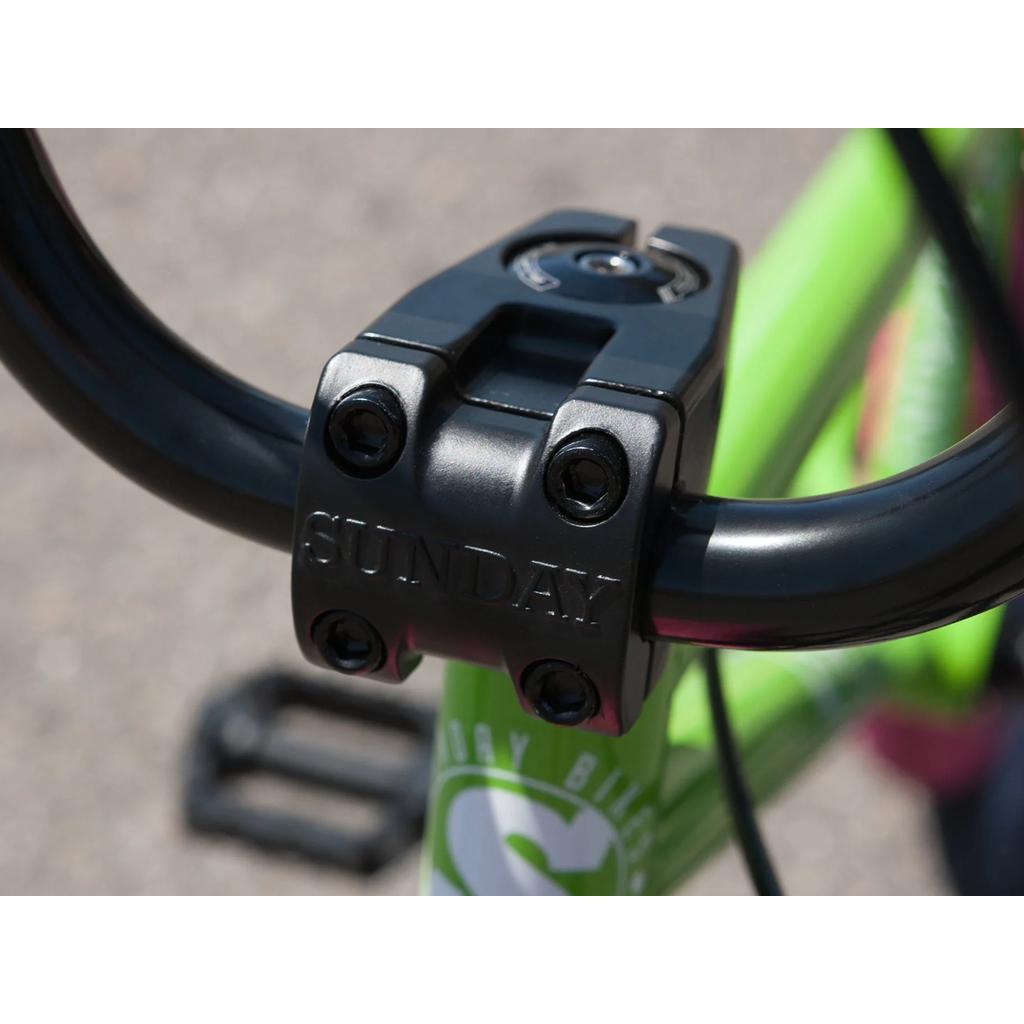 Close-up of the black stem on the Sunday Blueprint 20 Inch Bike (2023), engraved with "SUNDAY," attached to green handlebars and frame—engineered with pro-level geometry for precision riding.