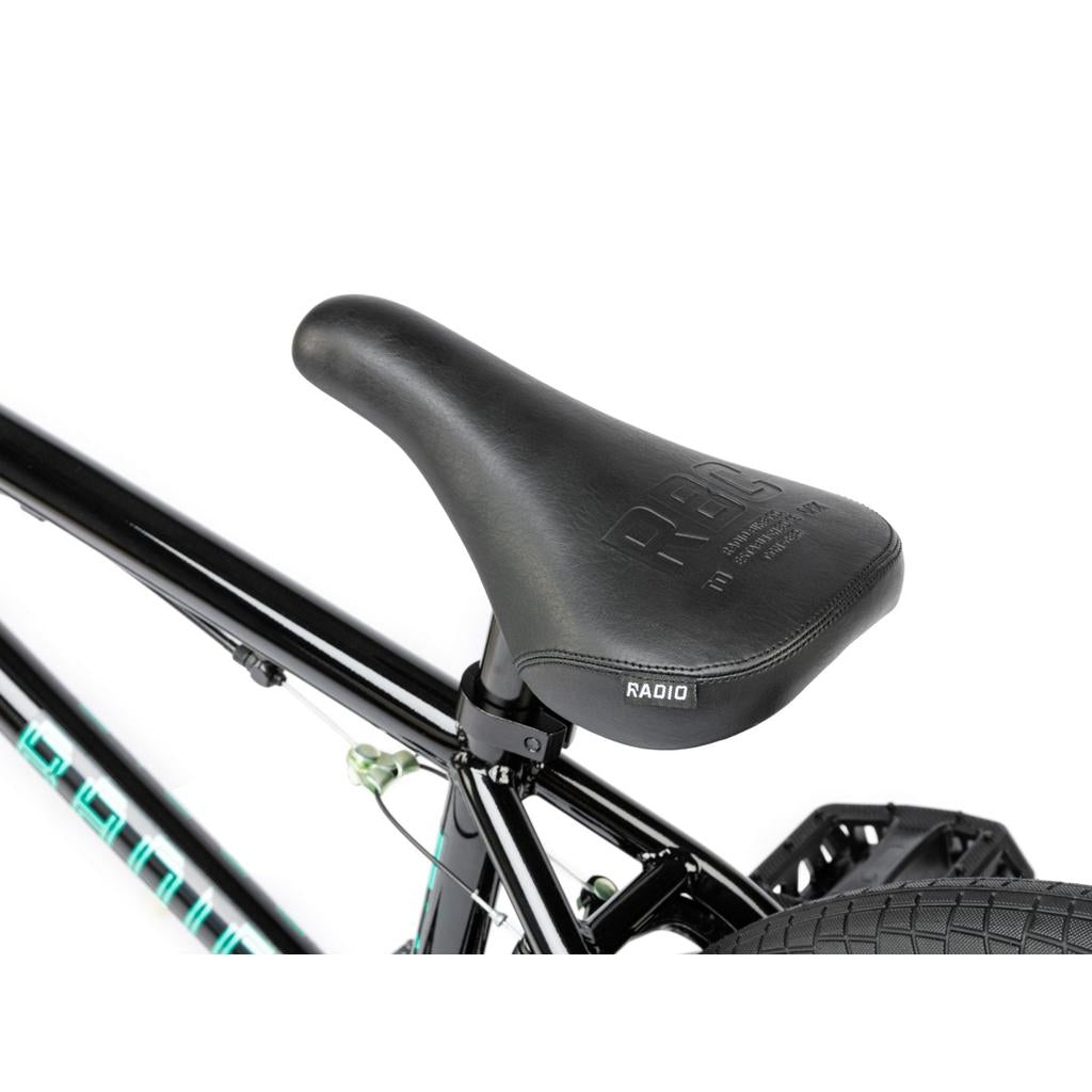 Close-up of a black BMX seat labeled "RBC" and "RADIO," mounted on a Radio Revo Pro FS 20 Inch Bike frame, showing the tire and part of the rear brake cable.