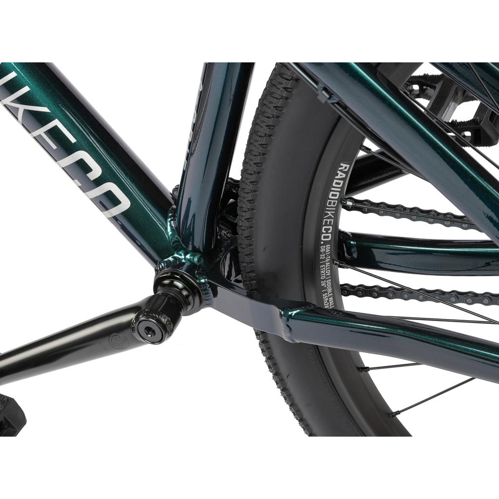 Close-up of the rear wheel, crank arm, and frame junction on a dark green Radio Griffin 26 Inch Bike with RADIOBIKECO branding on the tire and Maxxis DTH tyres.