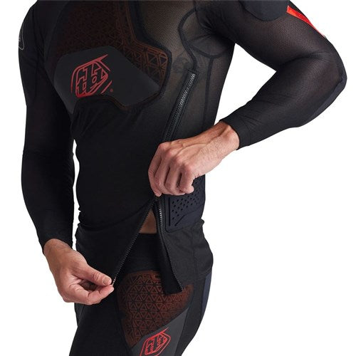 Person zipping up the TLD 26.1 Stage Ghost D30 LS Protective Shirt Baselayer, a black, form-fitting top with geometric patterns and red accents from our collection, featuring advanced underlayer protection.