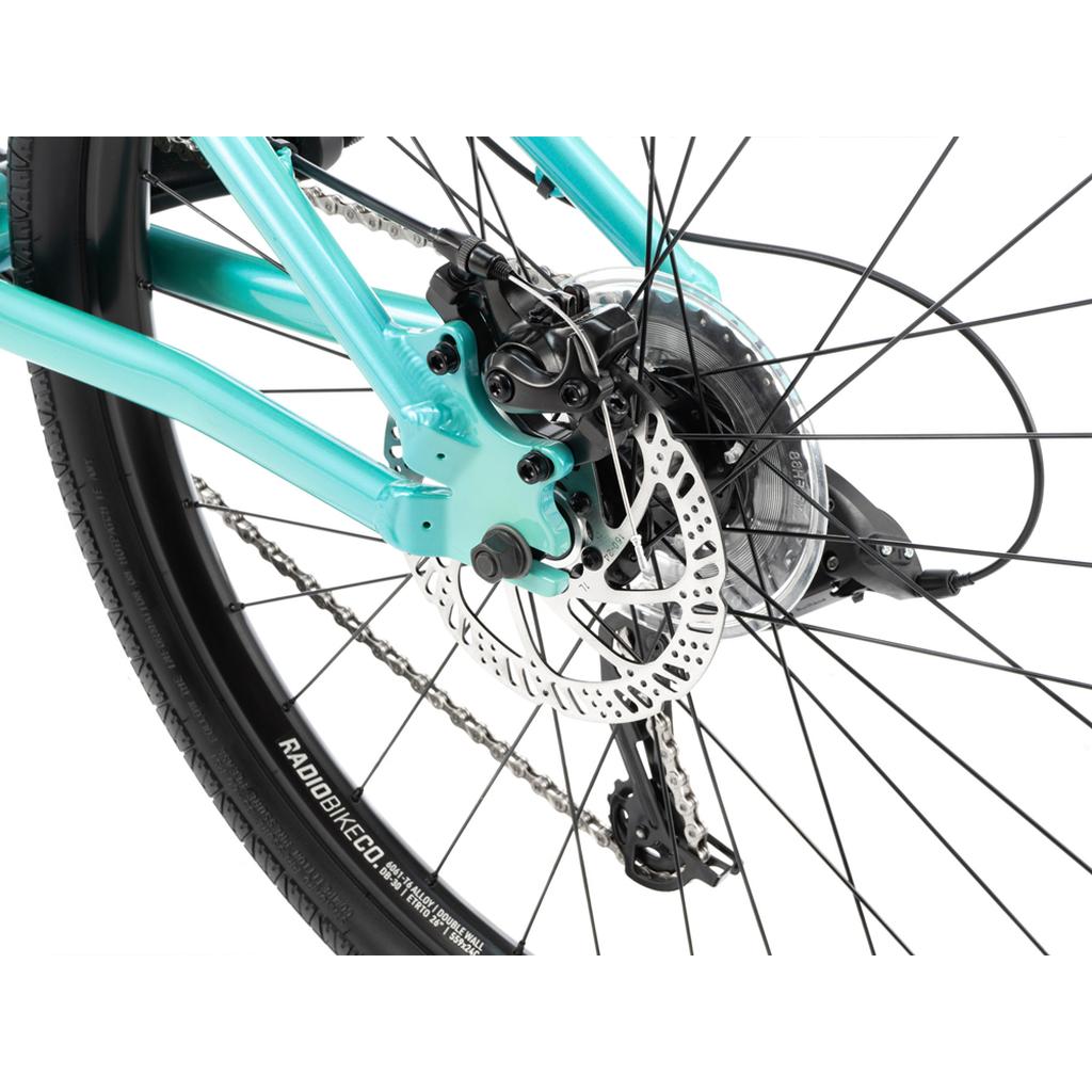 Close-up of the Radio Fiend 26 Inch Bike’s rear wheel, showcasing the disc brake, caliper, chain, and teal frame—a top pick for fans of alloy BMX or dirt jump bikes.