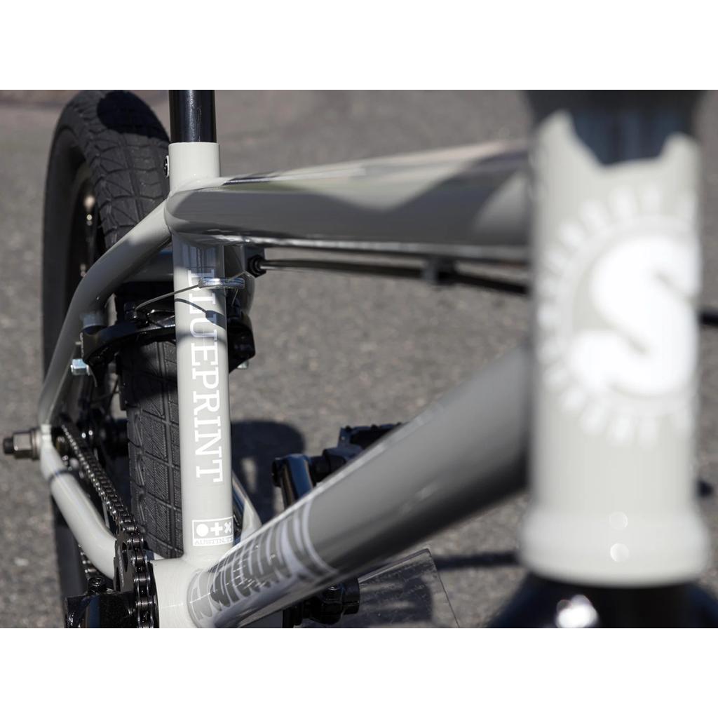 Close-up of the Sunday Blueprint 20 inch Bike frame in gray, displaying the word "BLUEPRINT" on the vertical tube, with portions of the tires and pedals visible—an excellent beginner BMX option equipped with Odyssey Springfield brakes.