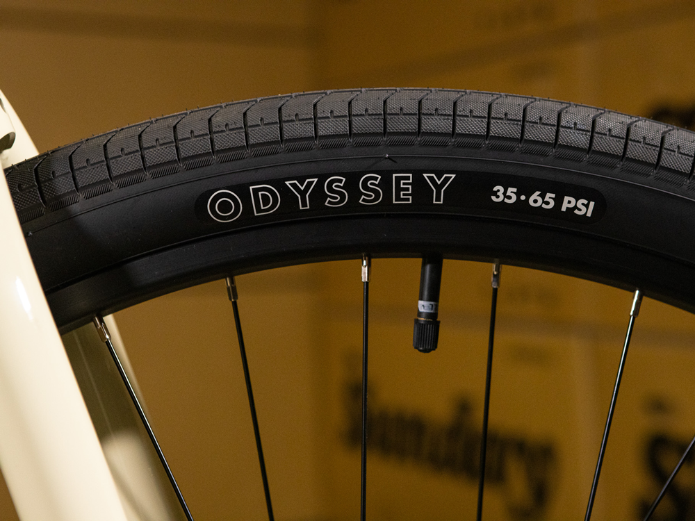 Close-up of a black Odyssey bicycle tire mounted on a wheel, revealing the tread, valve stem, and the 35-65 PSI pressure range printed on the sidewall—ideal for the Sunday High C 29 Inch Bike, which features a strong chromoly frame.