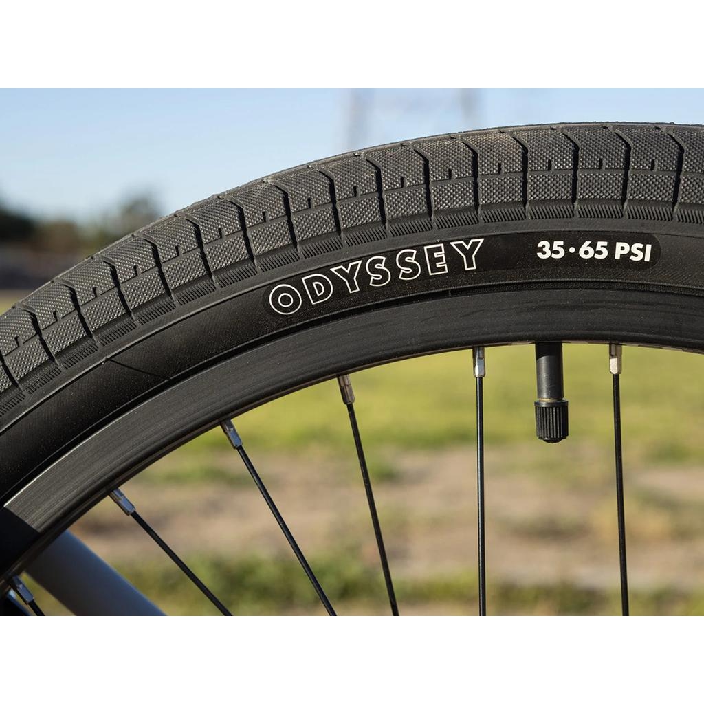 Close-up of a Sunday Model C 24 Inch Bike wheel with a black tire labeled "ODYSSEY" and "35-65 PSI," showing distinctive tread, spokes, and quality Odyssey Parts against a blurred outdoor background.