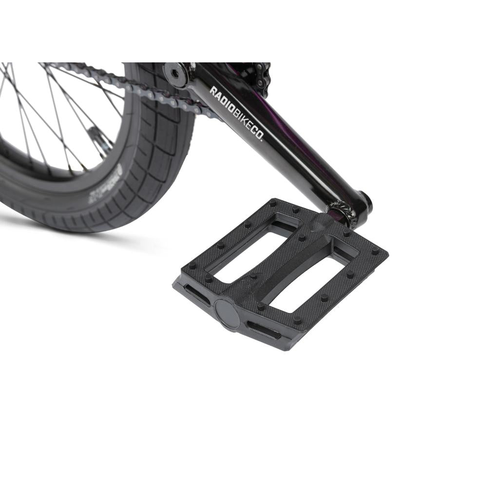 Close-up of a black pedal attached to a crank arm, with part of the rear wheel and chain visible on a Radio Saiko 20 Inch kids BMX bike.