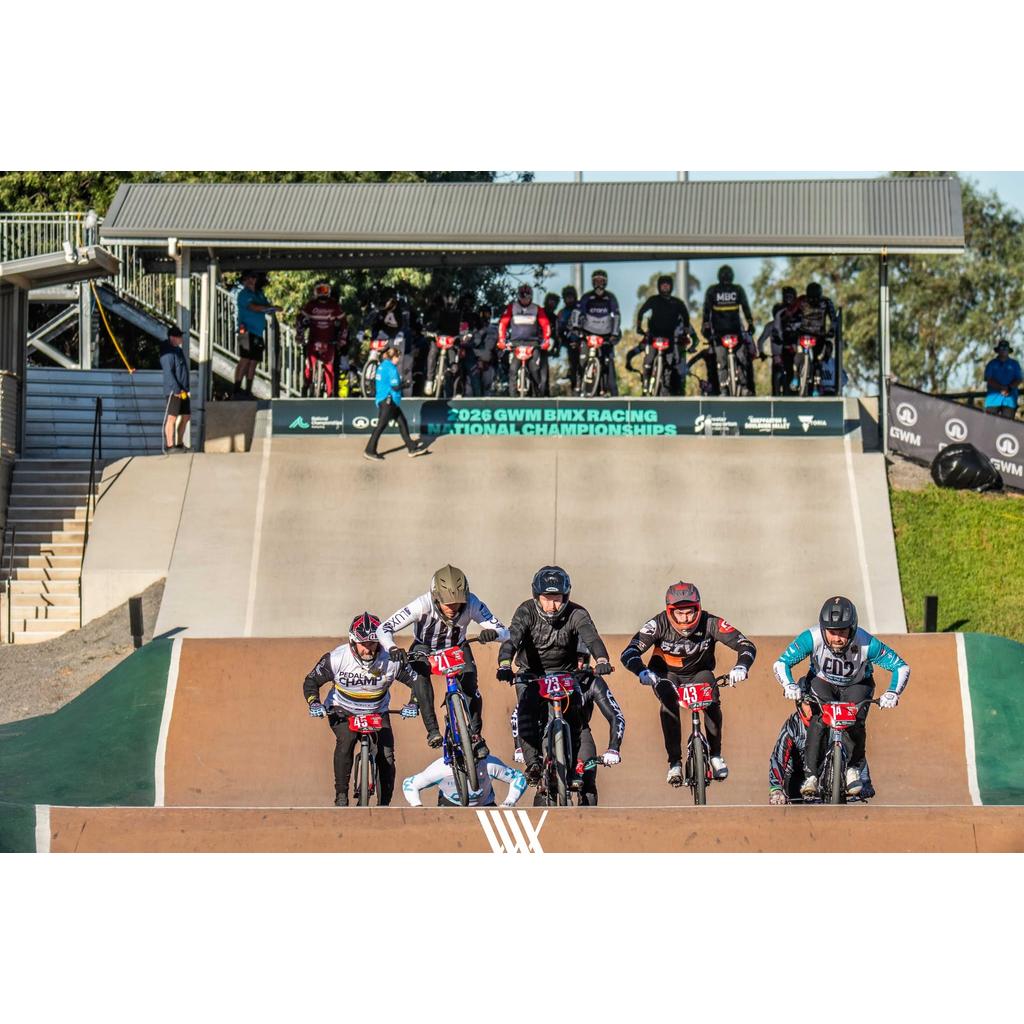 Five BMX riders race down a ramp at the 2024 BMX Racing National Championships, some powering ahead on their Inspyre EVO-C Pro Cruiser Race Bike (2027), while other competitors wait in the background.
